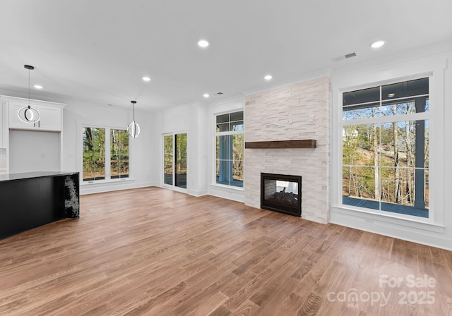 unfurnished living room with ornamental molding, a stone fireplace, and light wood-type flooring