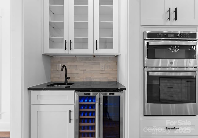 kitchen with wine cooler, white cabinets, double oven, and sink