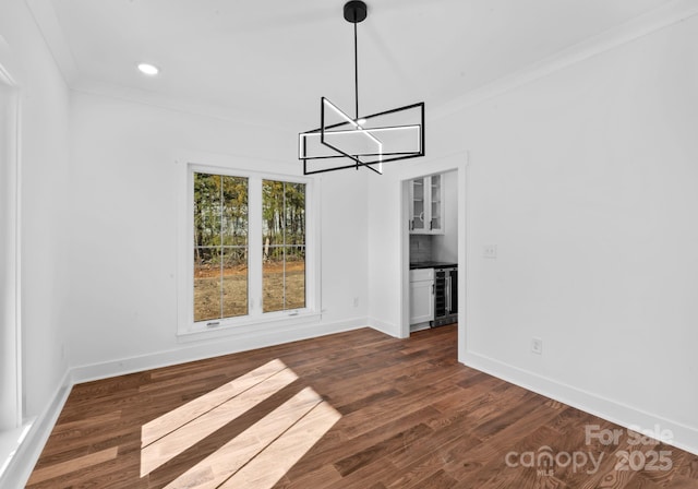 unfurnished dining area featuring dark wood-type flooring, ornamental molding, wine cooler, and an inviting chandelier