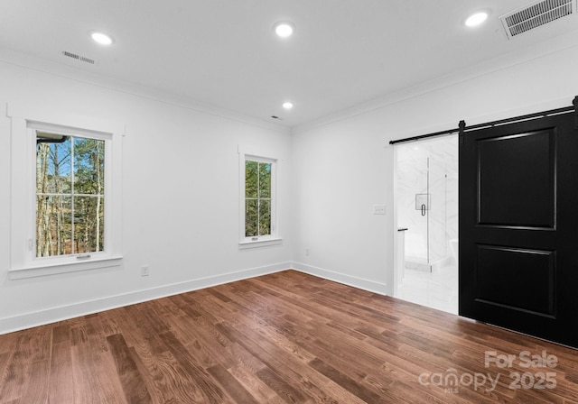 spare room featuring a barn door, crown molding, and hardwood / wood-style flooring