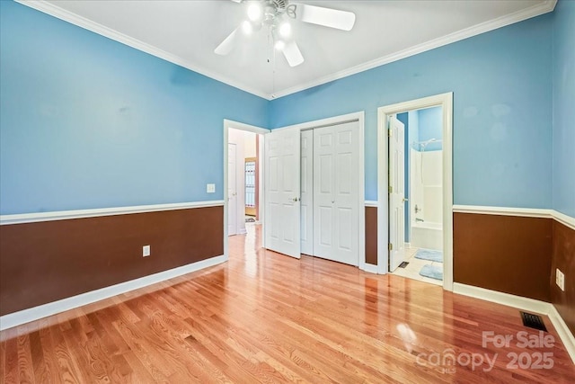 unfurnished bedroom featuring wood finished floors, visible vents, a closet, crown molding, and baseboards