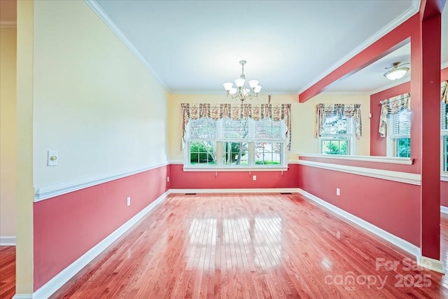 unfurnished dining area featuring wood finished floors, crown molding, baseboards, and an inviting chandelier