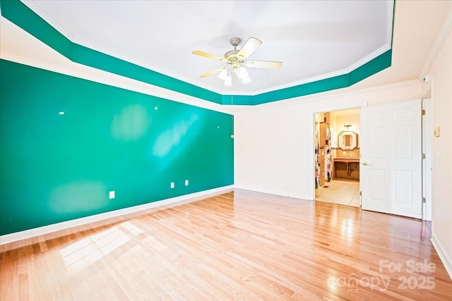 spare room featuring a ceiling fan, wood finished floors, a raised ceiling, baseboards, and ornamental molding