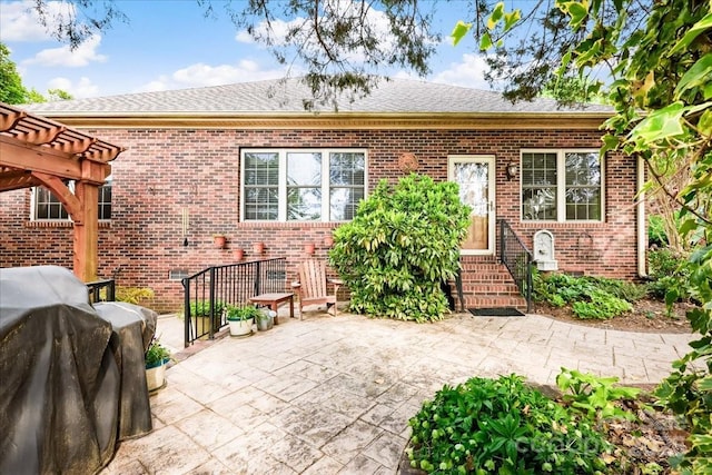 rear view of property featuring a pergola, a shingled roof, entry steps, a patio, and brick siding