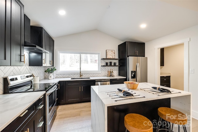 kitchen with wall chimney exhaust hood, a kitchen bar, stainless steel appliances, sink, and vaulted ceiling