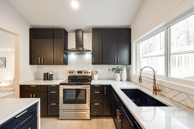 kitchen featuring stainless steel electric range oven, wall chimney range hood, backsplash, light stone countertops, and sink