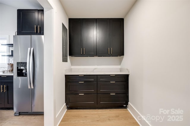 kitchen with light wood-type flooring, stainless steel refrigerator with ice dispenser, and light stone counters