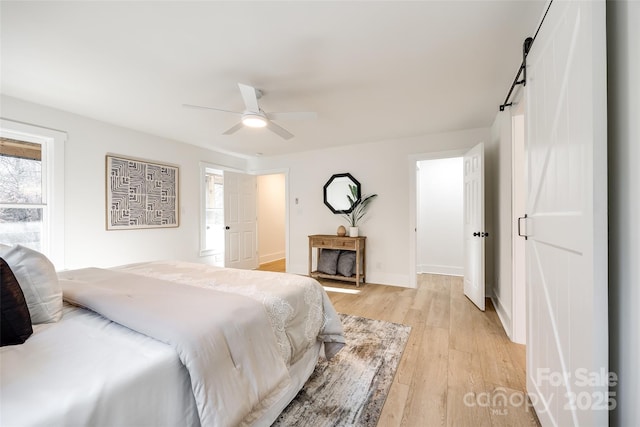 bedroom with light wood-type flooring, ceiling fan, and a barn door