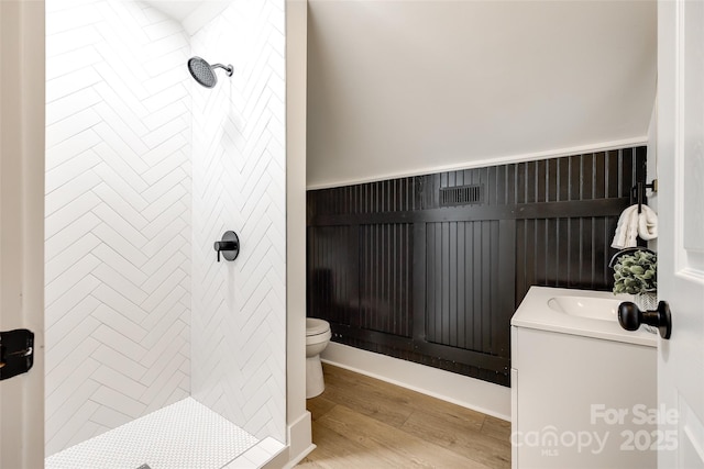 bathroom featuring toilet, a tile shower, hardwood / wood-style floors, and vanity