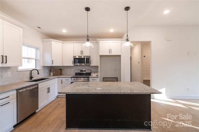 kitchen featuring stainless steel appliances, hanging light fixtures, a kitchen island, sink, and white cabinets