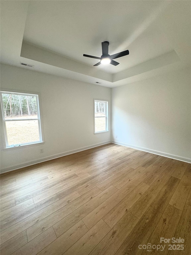 empty room with ceiling fan, light hardwood / wood-style flooring, and a raised ceiling