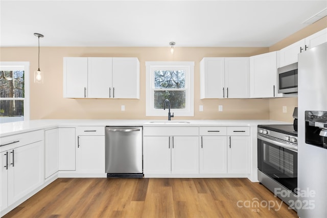 kitchen with light wood finished floors, light countertops, stainless steel appliances, white cabinetry, and a sink