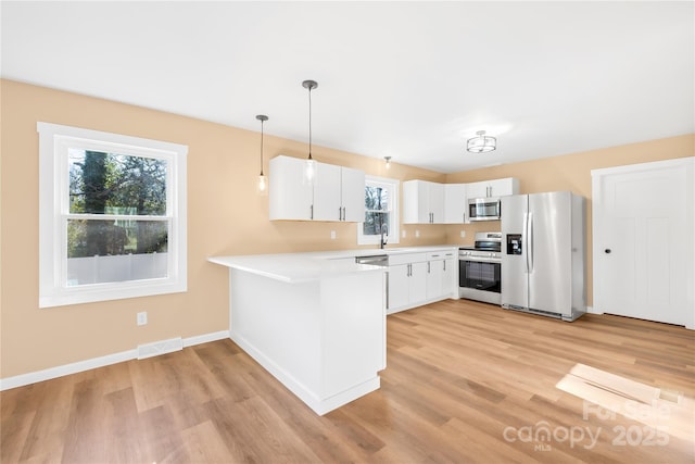 kitchen featuring visible vents, a peninsula, a sink, stainless steel appliances, and light countertops