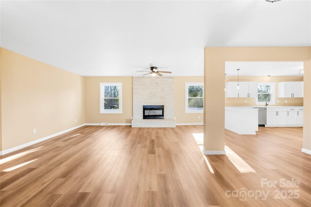 unfurnished living room featuring a brick fireplace, baseboards, ceiling fan, light wood-style flooring, and a sink