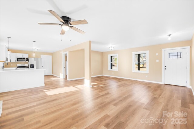 unfurnished living room featuring light wood-style flooring, a ceiling fan, baseboards, and a sink