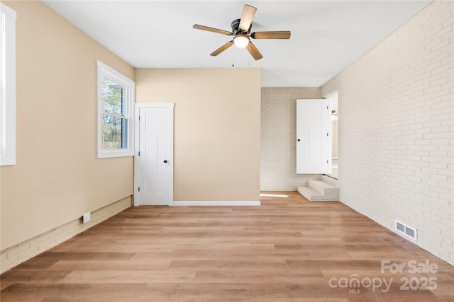 unfurnished room featuring ceiling fan, visible vents, brick wall, and light wood finished floors