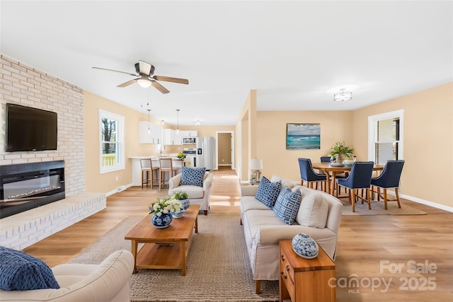 living room with ceiling fan, light hardwood / wood-style flooring, and a brick fireplace