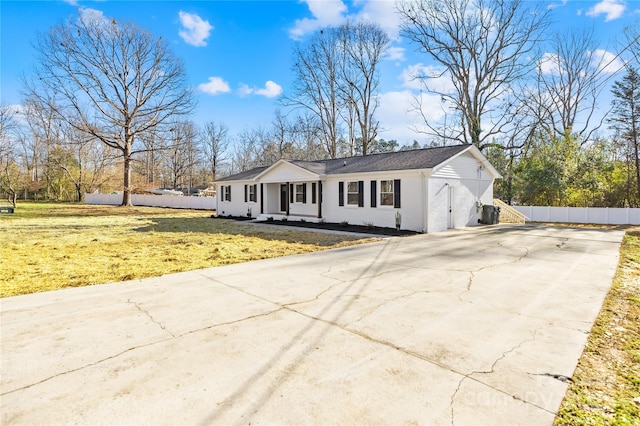 ranch-style home featuring concrete driveway, fence, and a front lawn