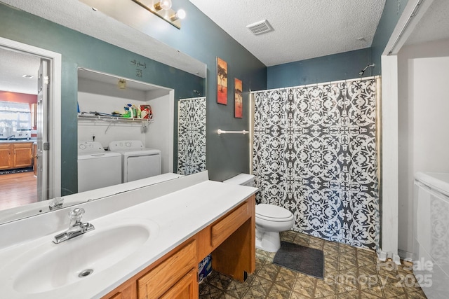 bathroom featuring a textured ceiling, toilet, washer and dryer, and vanity