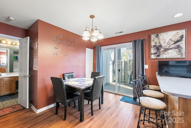 dining area with an inviting chandelier, a textured ceiling, and light hardwood / wood-style floors