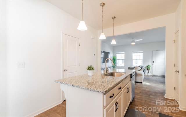 kitchen featuring decorative light fixtures, wood-type flooring, sink, a kitchen island with sink, and light stone counters