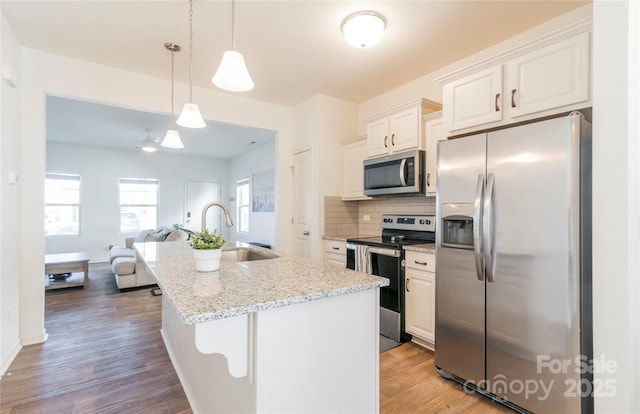 kitchen with hanging light fixtures, white cabinets, an island with sink, stainless steel appliances, and light stone counters