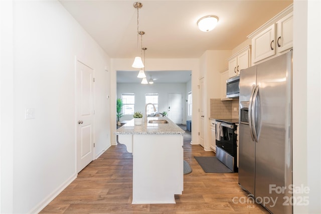 kitchen featuring light stone countertops, appliances with stainless steel finishes, decorative light fixtures, sink, and a center island with sink