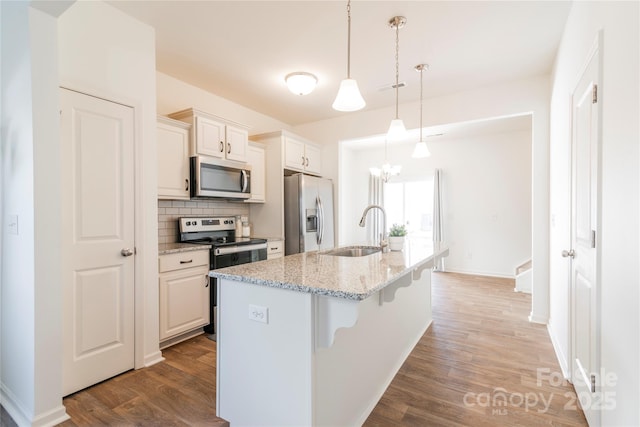 kitchen with a kitchen bar, stainless steel appliances, sink, light stone counters, and a center island with sink