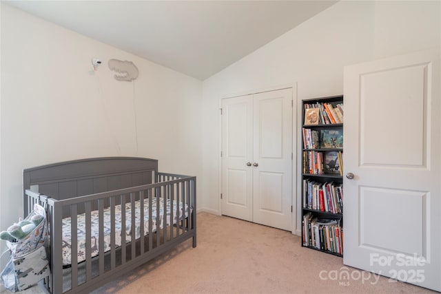 carpeted bedroom with a closet, lofted ceiling, and a crib