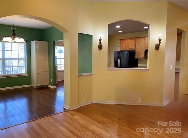 unfurnished living room with wood-type flooring, plenty of natural light, and an inviting chandelier