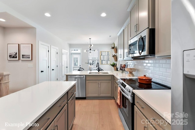 kitchen featuring stainless steel appliances, tasteful backsplash, sink, hanging light fixtures, and light hardwood / wood-style flooring