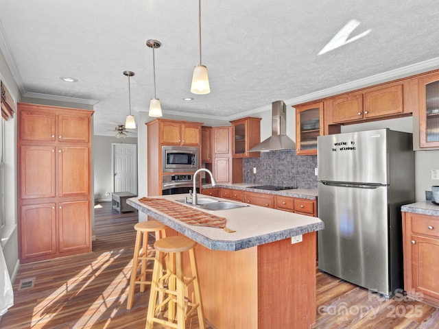 kitchen featuring crown molding, appliances with stainless steel finishes, a kitchen island with sink, and wall chimney range hood