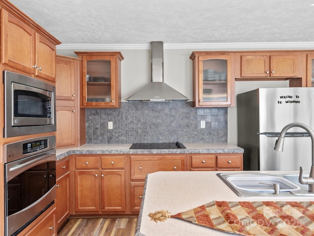 kitchen with stainless steel appliances, wall chimney exhaust hood, tasteful backsplash, crown molding, and light hardwood / wood-style flooring