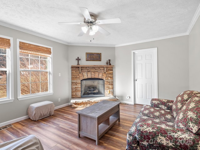 living room with ceiling fan, hardwood / wood-style flooring, a stone fireplace, a textured ceiling, and ornamental molding