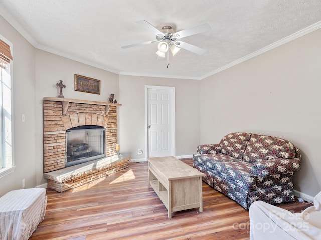 living room with ceiling fan, a fireplace, crown molding, light wood-type flooring, and a textured ceiling