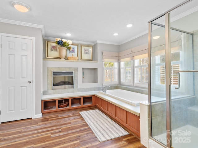 bathroom featuring a tiled fireplace, hardwood / wood-style floors, crown molding, and separate shower and tub