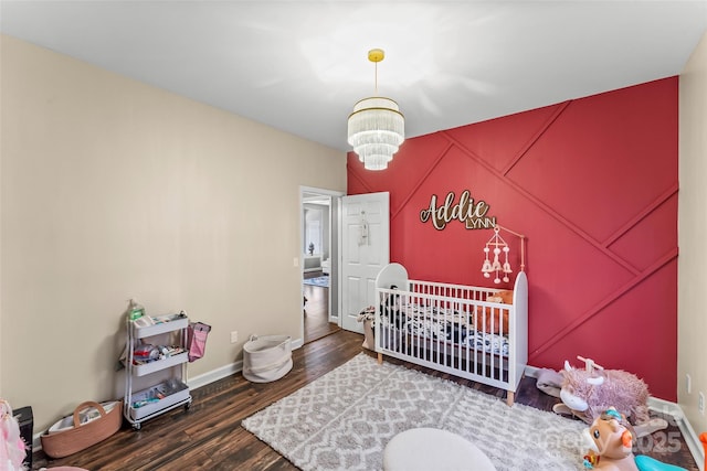 bedroom featuring a nursery area, an inviting chandelier, and dark wood-type flooring