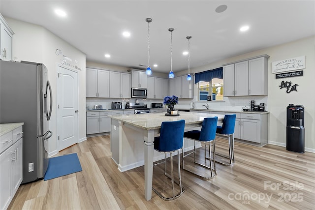 kitchen featuring decorative light fixtures, a center island, light stone counters, stainless steel appliances, and light hardwood / wood-style flooring