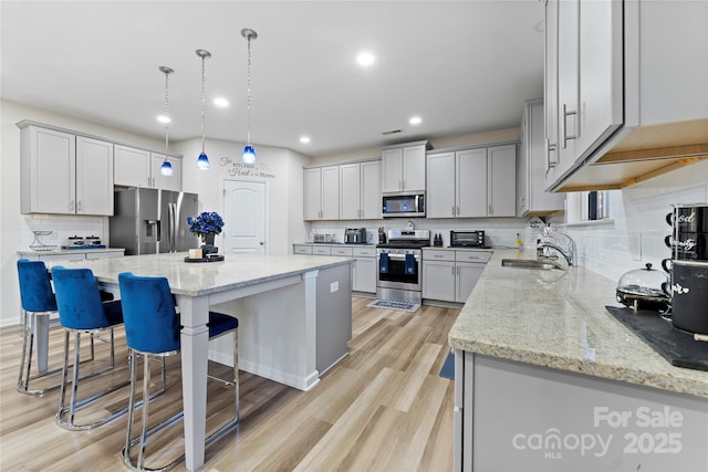 kitchen featuring sink, stainless steel appliances, tasteful backsplash, a kitchen island, and decorative light fixtures