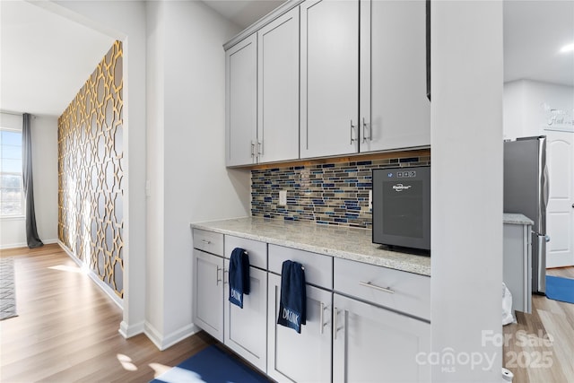 kitchen with stainless steel refrigerator, gray cabinetry, backsplash, light stone counters, and light wood-type flooring