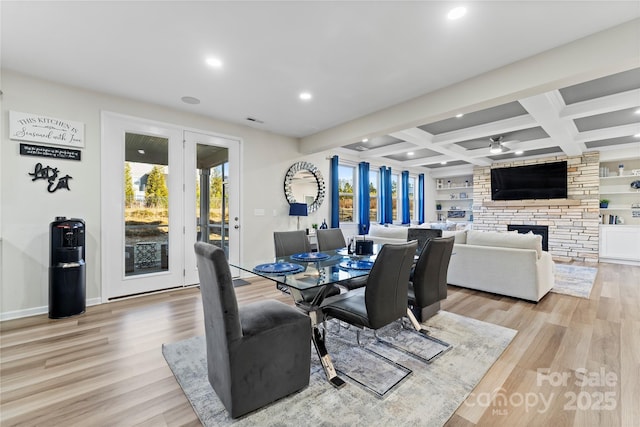 dining area with coffered ceiling, a stone fireplace, light wood-type flooring, ceiling fan, and beam ceiling