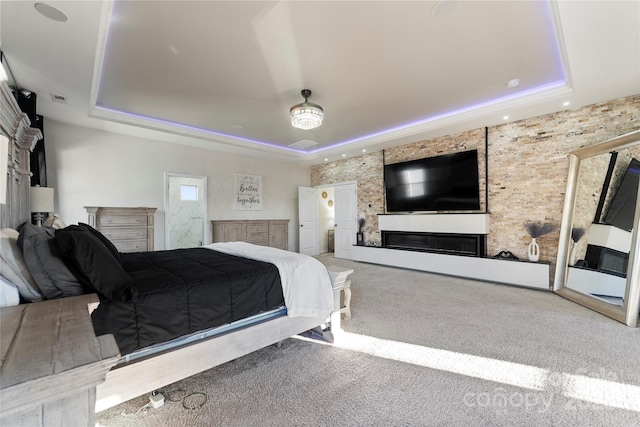 carpeted bedroom with a tray ceiling and a fireplace