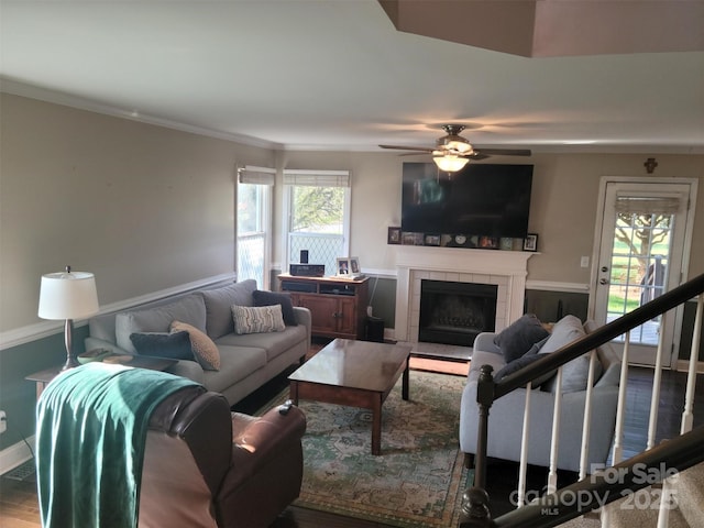 living area featuring ornamental molding, a healthy amount of sunlight, a tiled fireplace, and wood finished floors