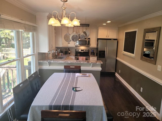 kitchen with ornamental molding, dark wood-style flooring, a peninsula, stainless steel appliances, and a sink