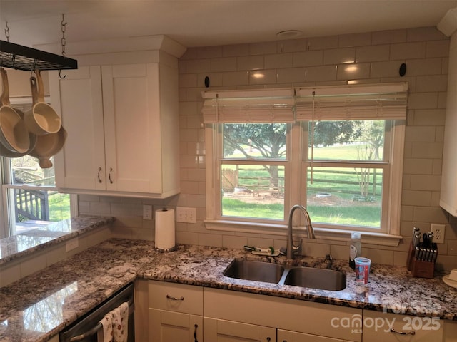 kitchen with white cabinets, dishwashing machine, light stone counters, a sink, and backsplash