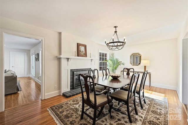 dining area with baseboards, a fireplace, wood finished floors, and a notable chandelier