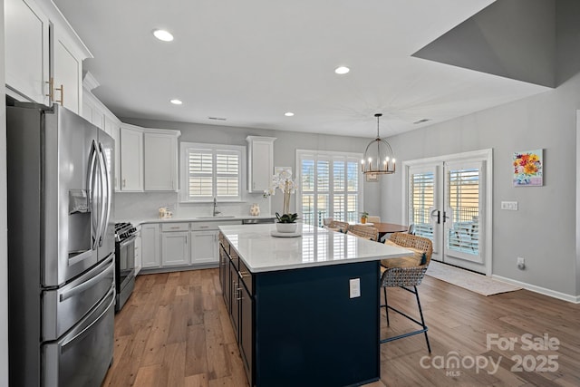 kitchen with appliances with stainless steel finishes, decorative light fixtures, french doors, white cabinets, and a center island