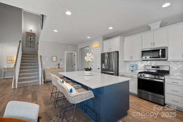 kitchen with white cabinets, appliances with stainless steel finishes, a center island, a kitchen bar, and tasteful backsplash