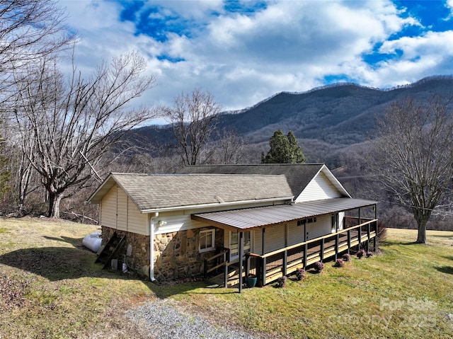 view of front facade with stone siding, a front yard, a mountain view, and roof with shingles