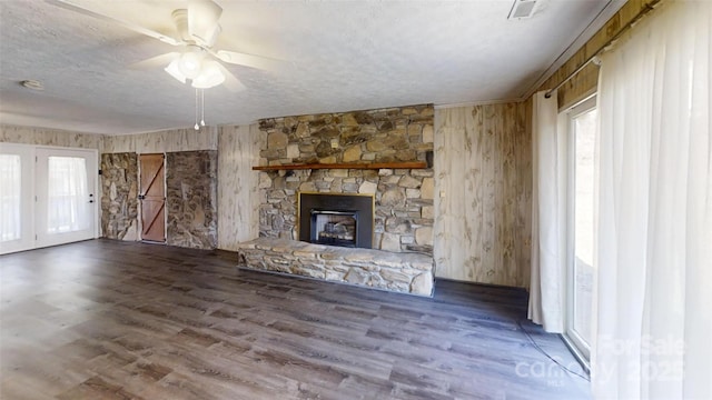 unfurnished living room featuring wood walls, a fireplace, a textured ceiling, and wood finished floors